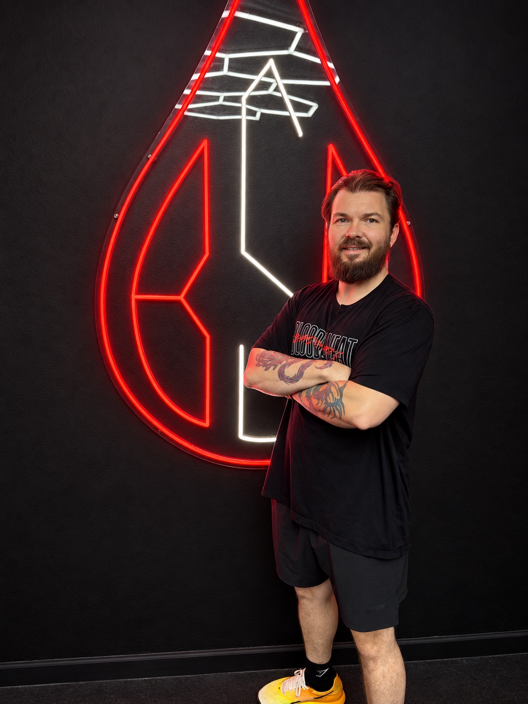 Adam Young standing in front of the Blood Sweat & Bodywork logo